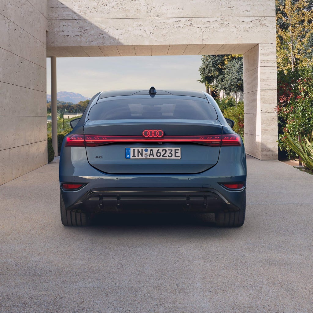Heckansicht eines blauen Audi Sportback A6 e-tron mit leuchtendem Lichtband, unter Betonvordach.