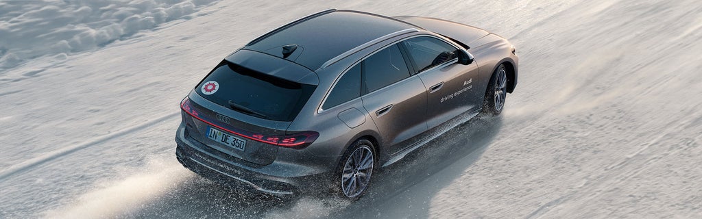 Silberner Audi S5 Avant mit „Audi driving experience“-Beschriftung fährt dynamisch über eine schneebedeckte Teststrecke bei Tageslicht.