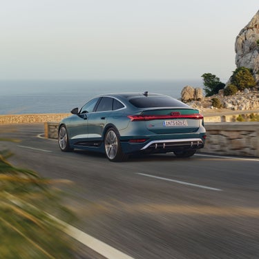 Ein grüner Audi S6 Sportback e-tron fährt an einer Küstenstraße entlang, im Hintergrund das Meer und Felsen.