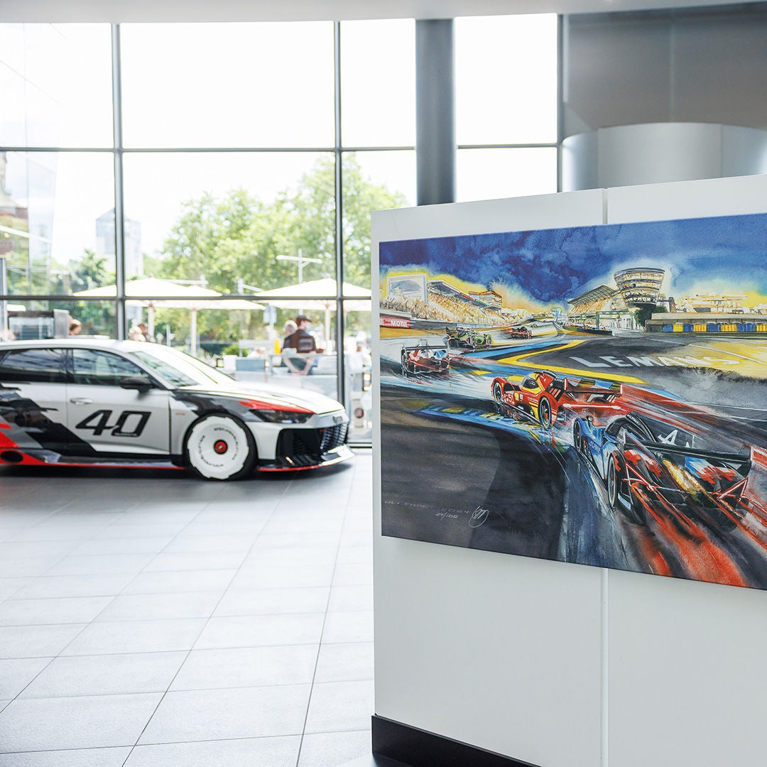 Gemälde einer Le-Mans-Rennszene im Vordergrund, dahinter ein Audi Rennfahrzeug mit Startnummer 40 in einer Ausstellungshalle.