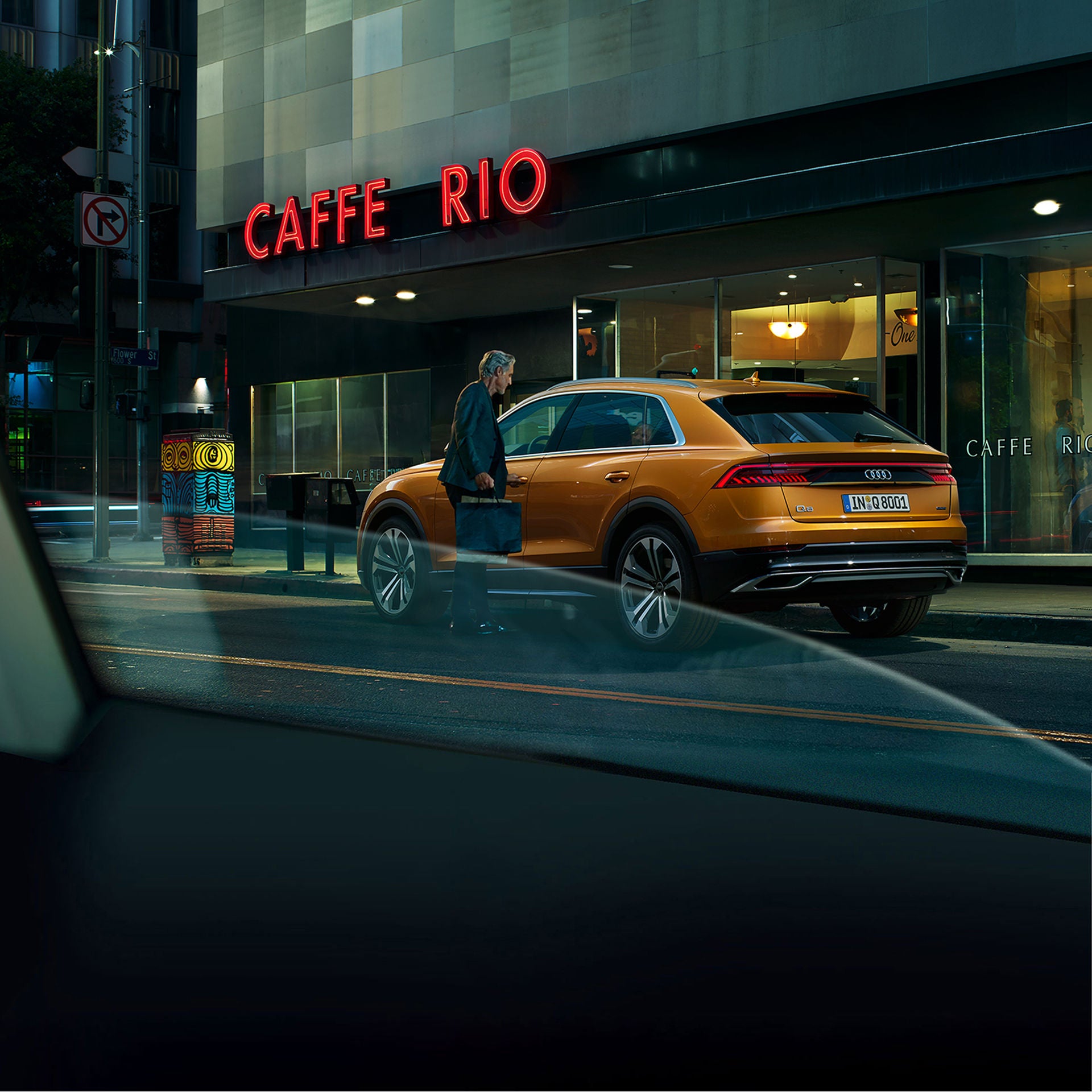 En man som står bredvid en gul Audi Q8 framför ett café