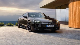 A sleek black Audi car parked outside a modern building, surrounded by greenery and a scenic backdrop of cloudy skies.