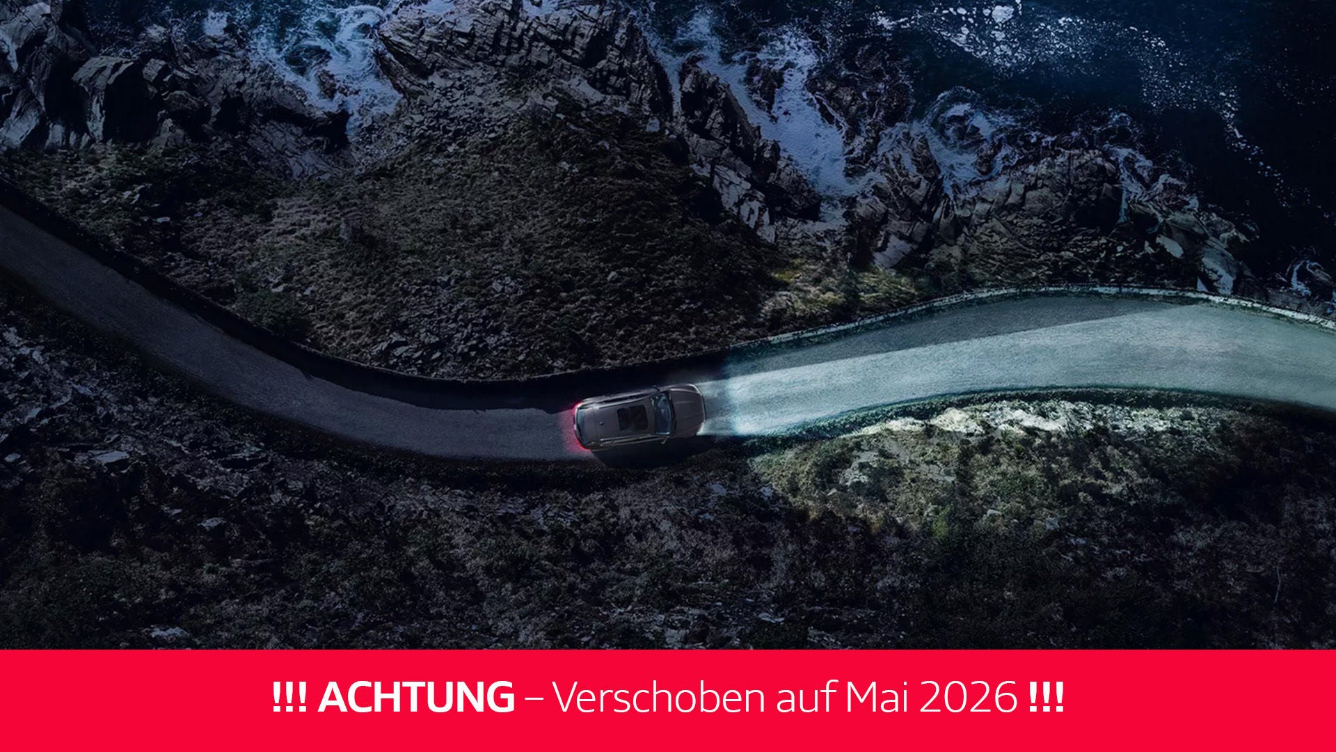 Auto mit eingeschaltetem Licht fährt bei Dunkelheit auf einer Küstenstraße entlang steiler Felsen und Wellen (mit rotem Störer Achtung: Verschoben auf Mai 2026).