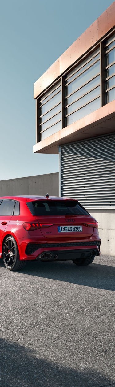 Rote Audi RS 3 Limousine parkt vor modernem Betongebäude bei Tageslicht.