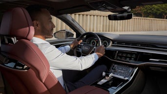 A man in the driver seat of an Audi car holding the steering wheel
