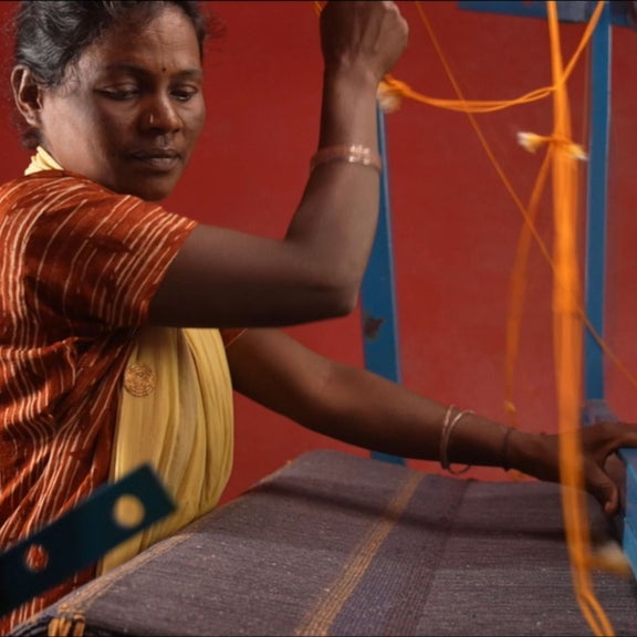Eine Frau im Close up an einem Webstuhl bei der Arbeit.