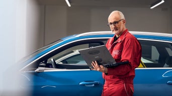 An Audi technician stood beside a parked Audi vehicle and using a laptop