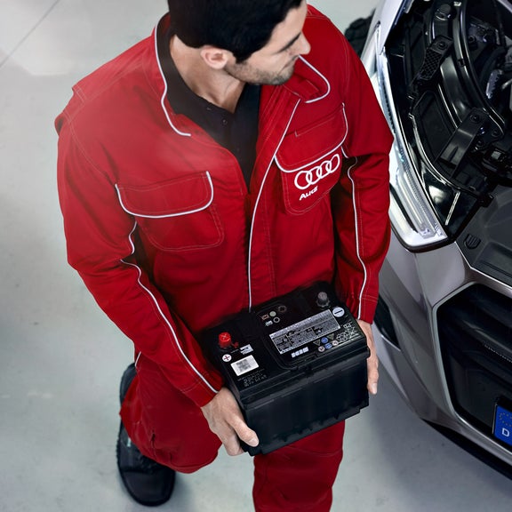 Närbild på en av Audis servicepersonal som bär på ett startbatteri