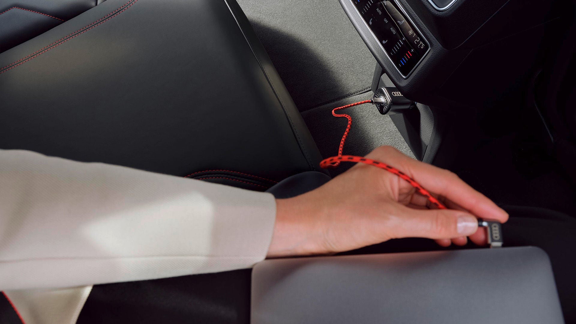 Hand steckt rotes Audi-Ladekabel in Gerät im Fahrzeuginnenraum mit schwarzem Leder und roten Ziernähten.
