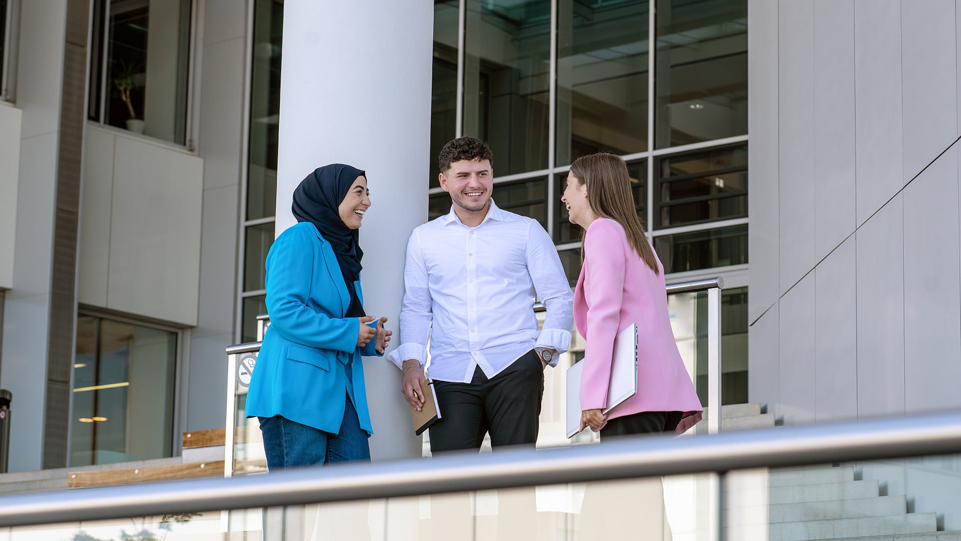 Drei Studenten stehen vor einem Gebäude und lachen zusammen