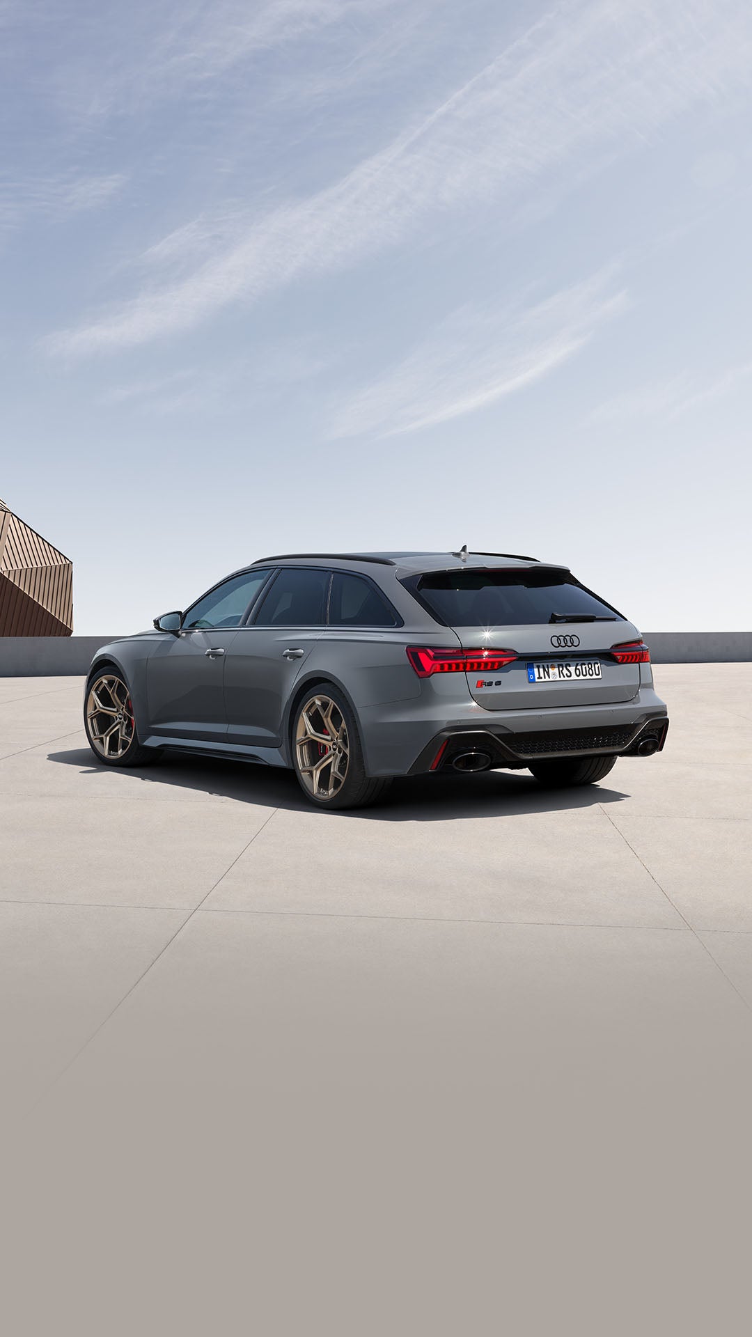 Mattgrauer Audi RS 6 Avant performance auf Platz, Mann im Anzug nähert sich, modernes Gebäude mit goldfarbener Fassade im Hintergrund.