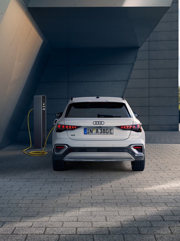 Heckansicht eines weißen Audi A3 allstreet TFSI e an Ladesäule mit gelbem Kabel.