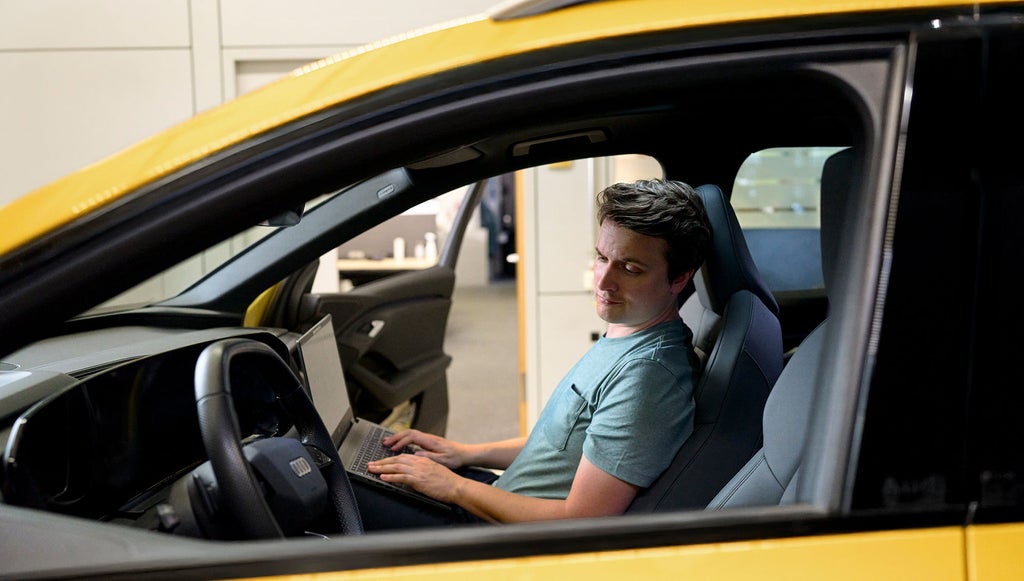 Jan Totz is sitting in the passenger seat of an Audi with a laptop on his lap, looking at the steering wheel