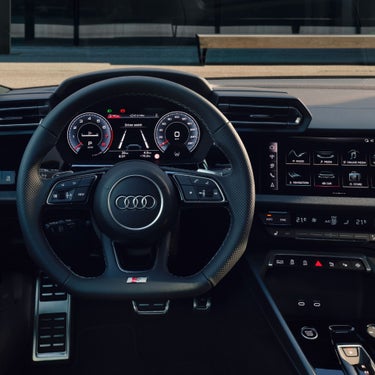 Interior view of an Audi vehicle focusing on the steering wheel with dashboard and infotainment system visible.