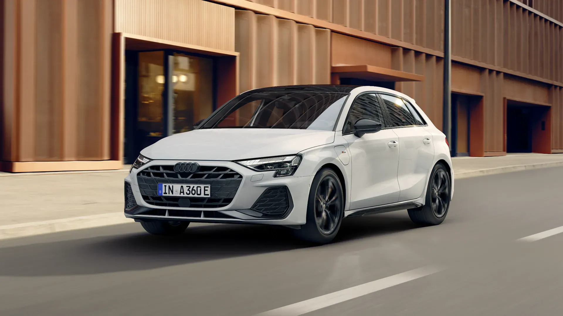 White Audi A3 Sportback e-hybrid driving on an urban street past modern buildings