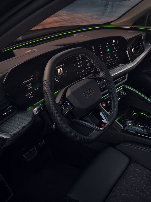 Digitales Cockpit eines Audi Q5 SUV mit zwei großen Displays und grünem Ambientelicht, durch die Frontscheibe sieht man grüne Bäume.