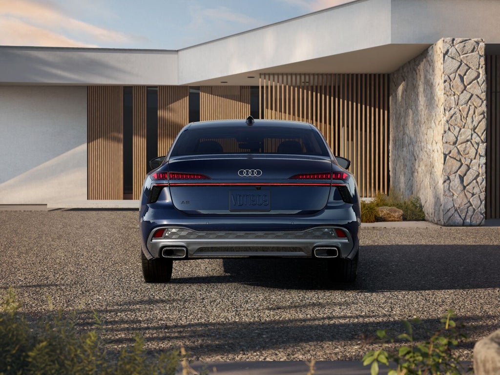 Un auto Audi A6 Sedán visto desde atrás se encuentra frente a una casa con revestimiento de madera.