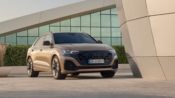 Ein goldener Audi Q8 SUV steht vor einem modernen Gebäude, frontal leicht von der Seite gezeigt.