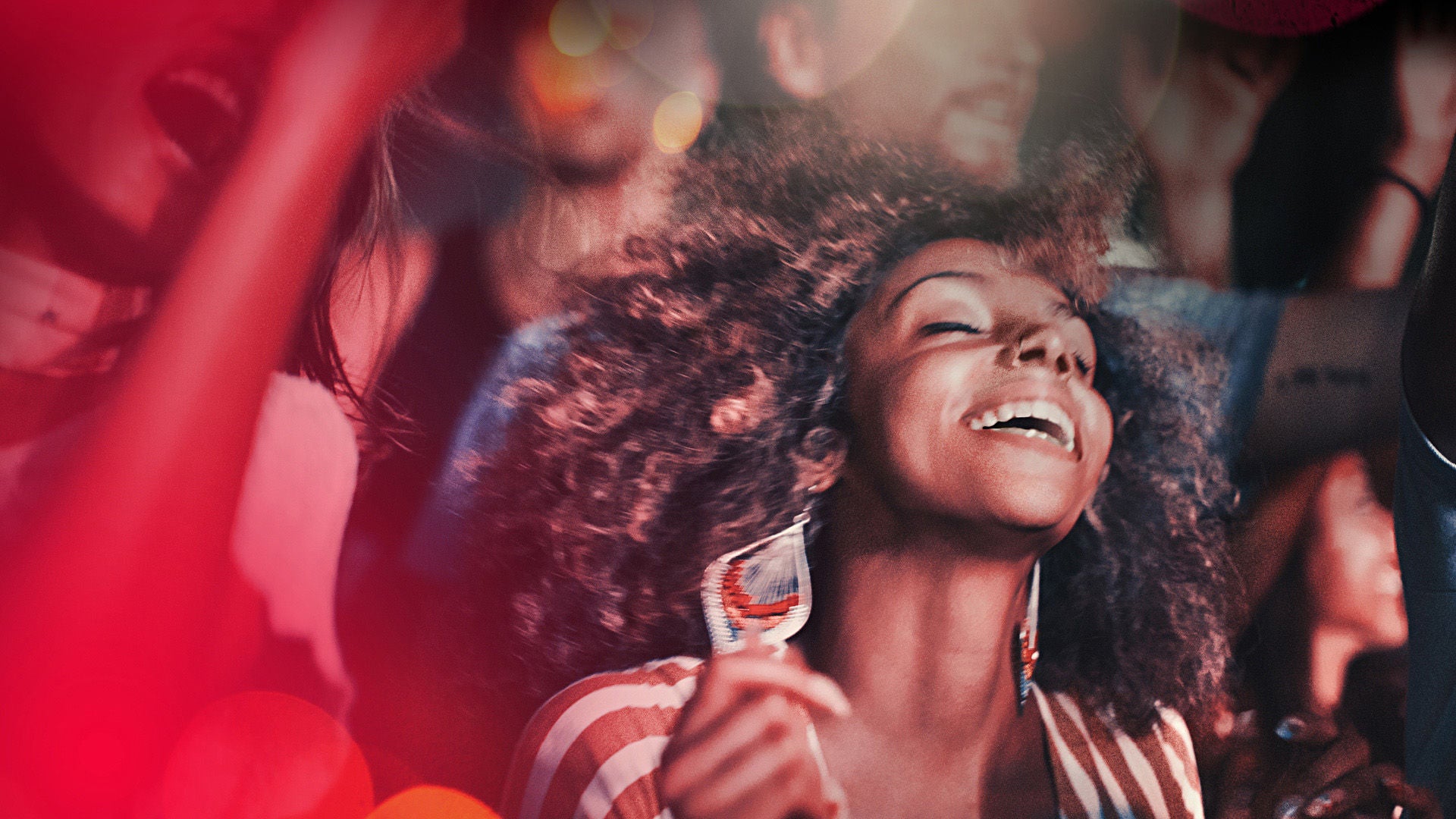 Frau mit lockigen Haaren und großen Ohrringen tanzt ausgelassen in der Menge.