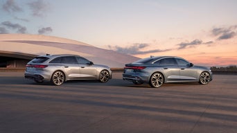 Deux voitures Audi A5, un break gris et une berline grise, sont garées côte à côte dans une rue. En arrière-plan, le ciel est rose et orange.