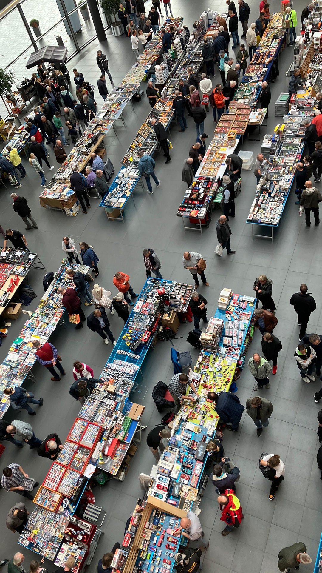 Draufsicht auf die Modellautoboerse 2023 im Audi Forum Neckarsulm. Aufgereihte Tische  im Foyer des Audi Forums präsentieren Modellautos zwischen den Tischen gehen Menschen und schauen sich die Modelle an.