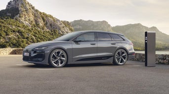 A6 Avant e-tron sett fra siden er tilkoblet en ladestasjon på en parkeringsplass ved en innsjø. Skogkledde fjell er synlige i bakgrunnen.