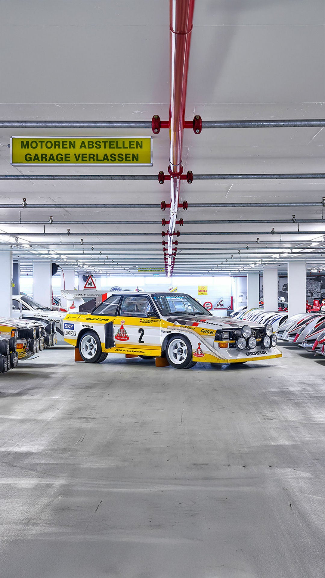 A classic Audi Quattro racing car in a garage, surrounded by other Audi racing cars.