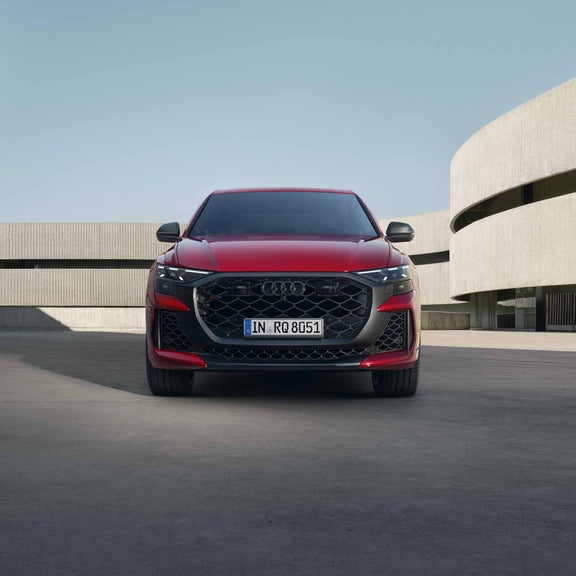 Frontansicht eines roten Audi RS Q8 SUV performance auf heller Betonfläche vor moderner Gebäudearchitektur bei Tageslicht.