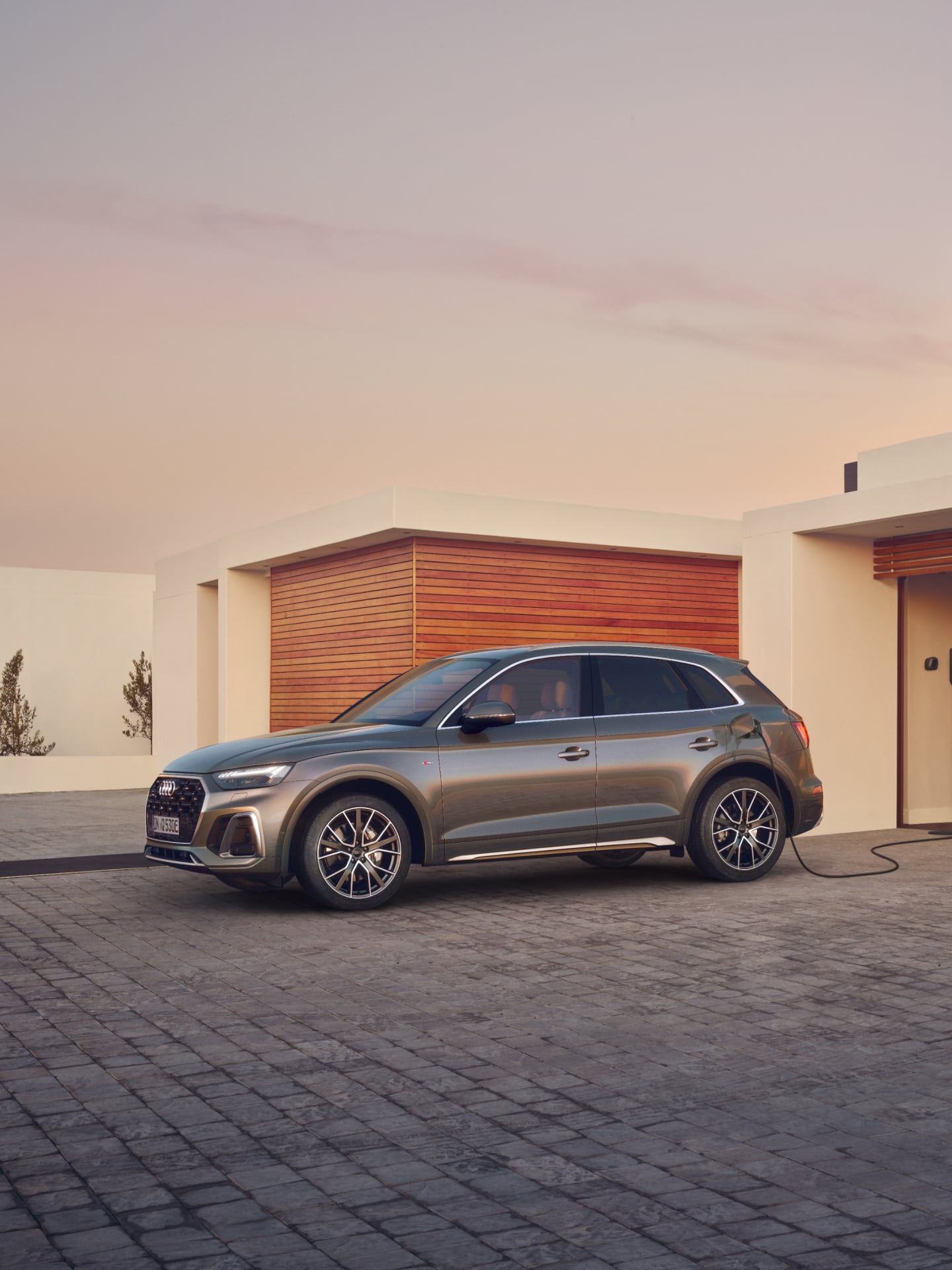 SUV charging at a modern home driveway during sunset.