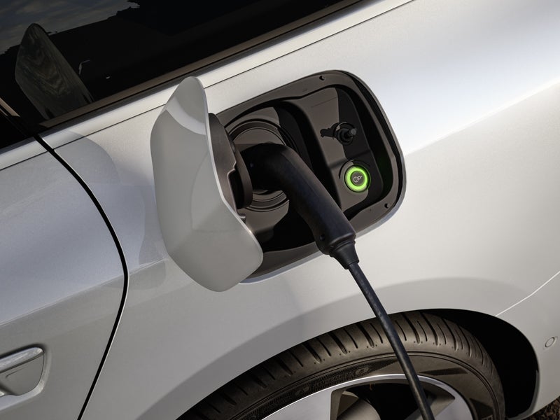 En svart laddkabel förvaras i ladduttaget på A6 Avant e-hybrid. Bredvid ladduttaget indikerar en symbol med en ljusgrön kant att laddningen pågår.