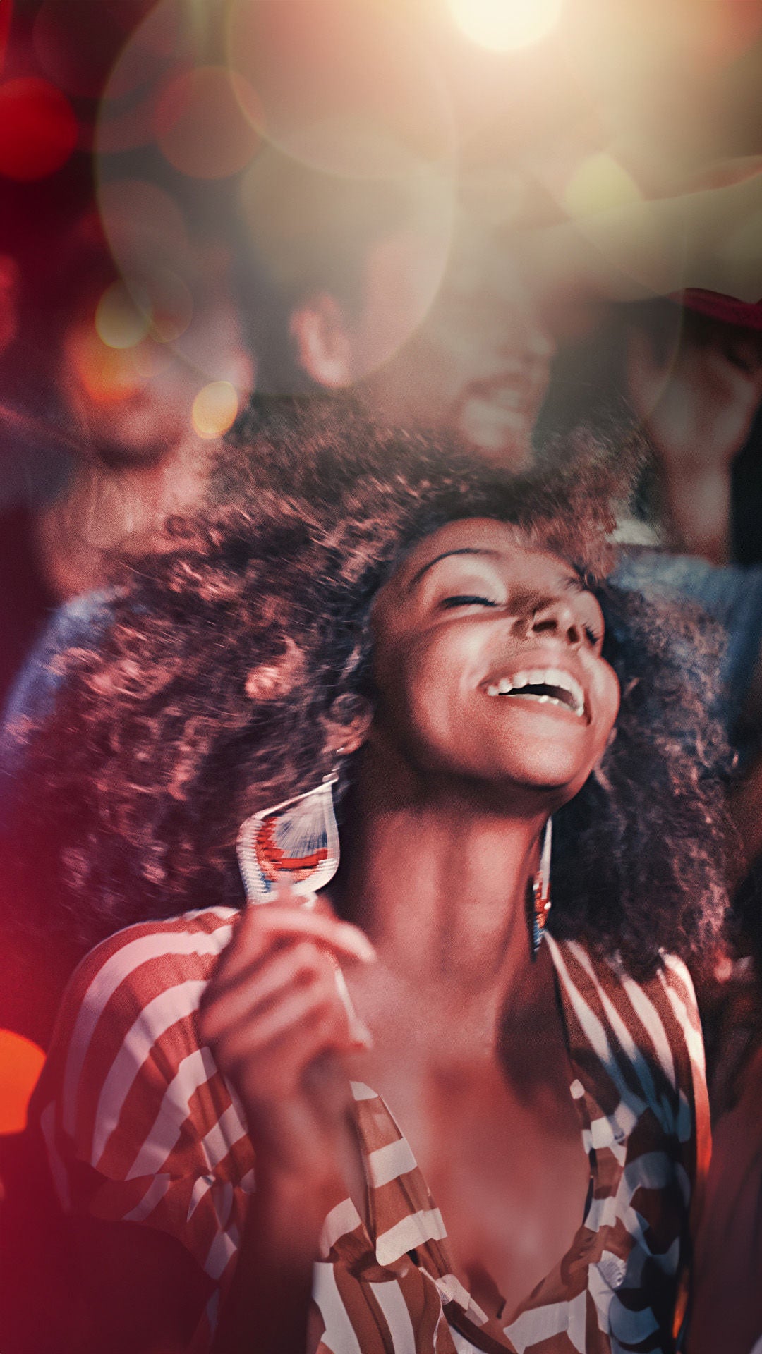 Frau mit großen Ohrringen und lockigem Haar ausgelassen beim Tanzen.