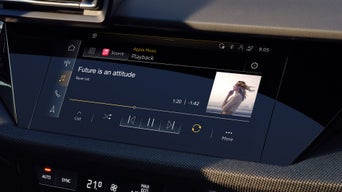 Hand hält Smartphone mit Fahrzeugsteuerungsmenü vor einem Audi-Fahrzeug mit unscharfem Kühlergrill.