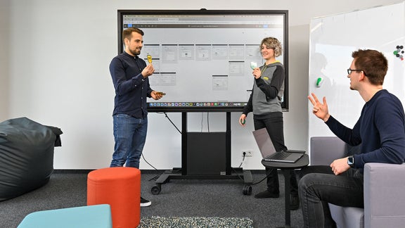 Nadine, Software Engineer SDC, hat ein Meeting mit Kollegen und hält einen Zettel hoch