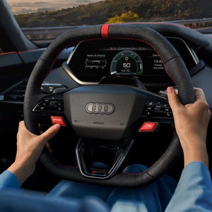 Twee vrouwelijke handen grijpen het stuur van de Audi RS e-tron GT vast.  De linkerduim drukt op de rode boostknop.