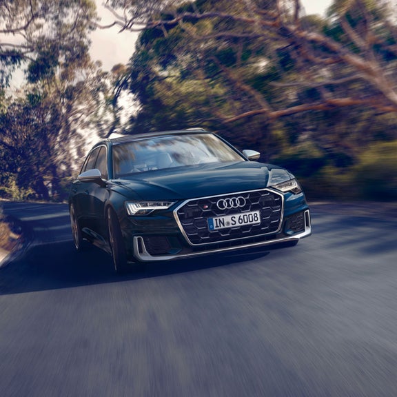 An Audi car navigates a winding road, showcasing its sleek design and dynamic performance in a scenic landscape.