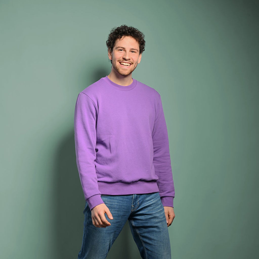 Fabian schaut in die Kamera und lacht. Er trägt einen lilanen Pullover