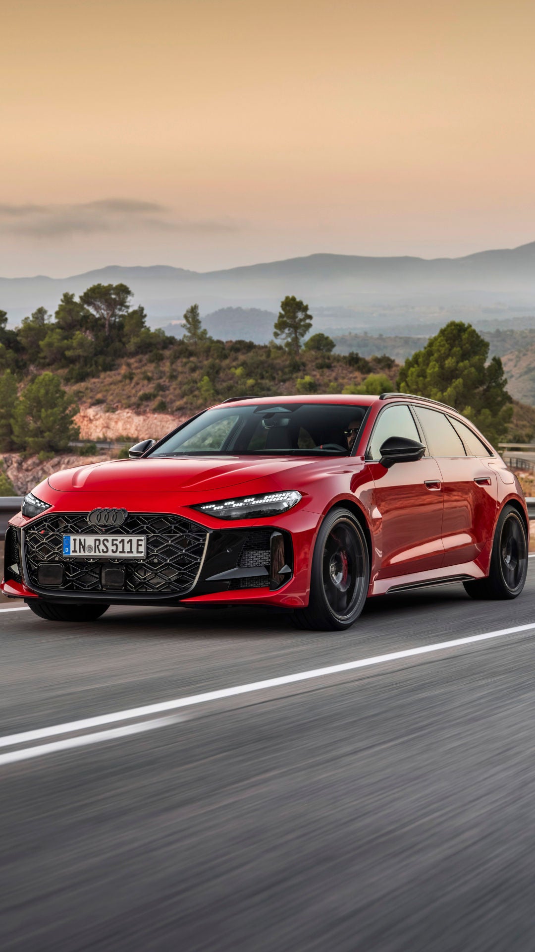 Audi RS5 Avant in der Farbe Progressivrot Metallic fährt auf einer Landstraße mit Bergen im Hintergrund