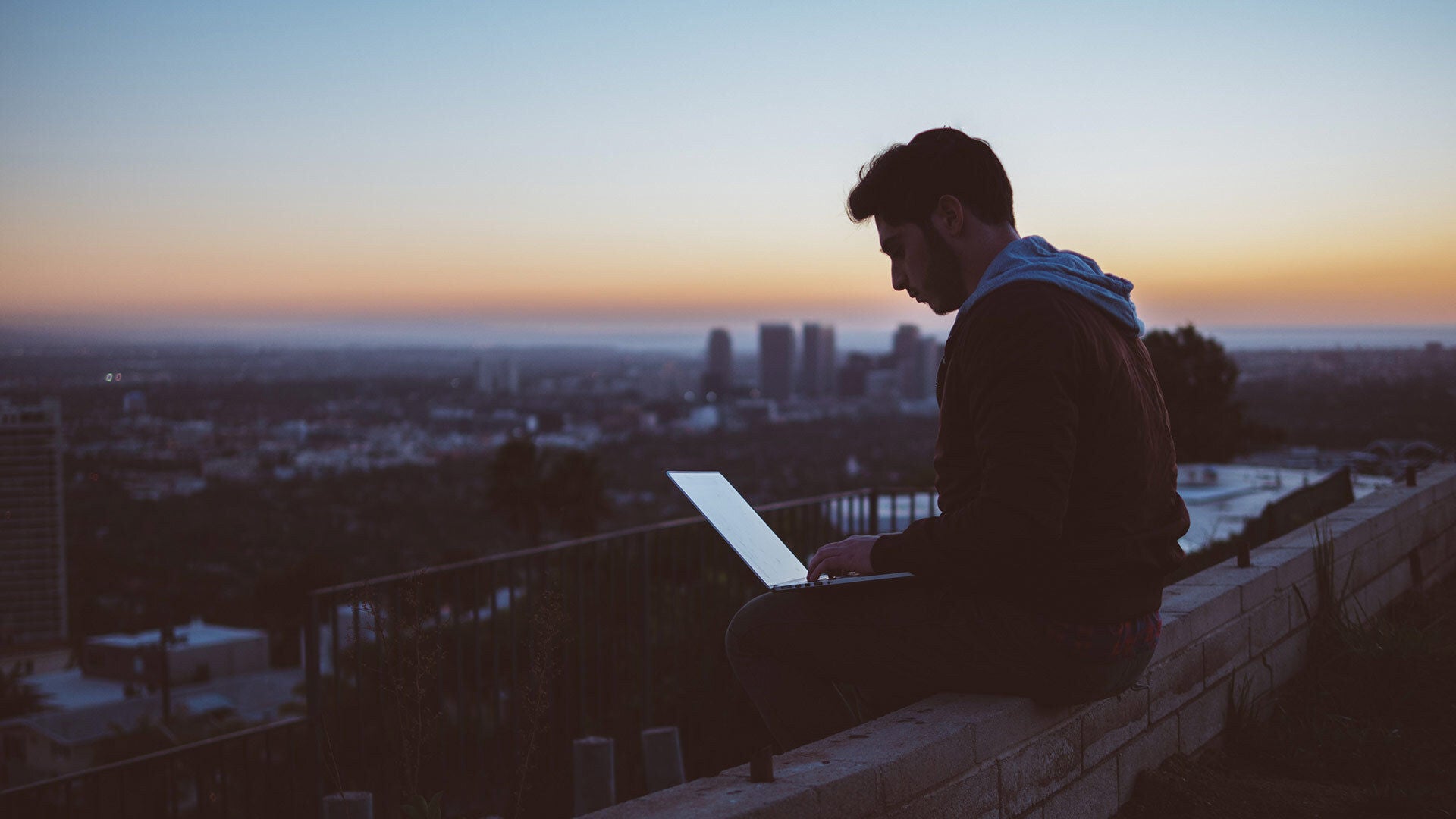 Mann mit Laptop sitzt auf einer Mauer