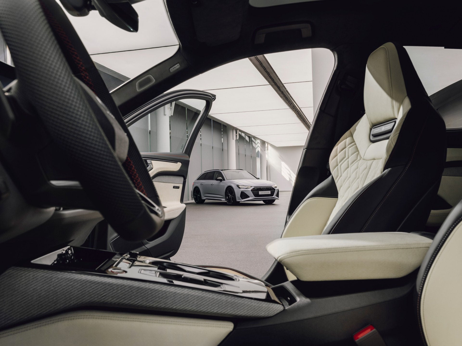 Door het geopende portier van een Audi A6 Avant met Audi exclusive-interieur is een Audi RS 6 Avant in Audi exclusive Pijlgrijs mateffect te zien.