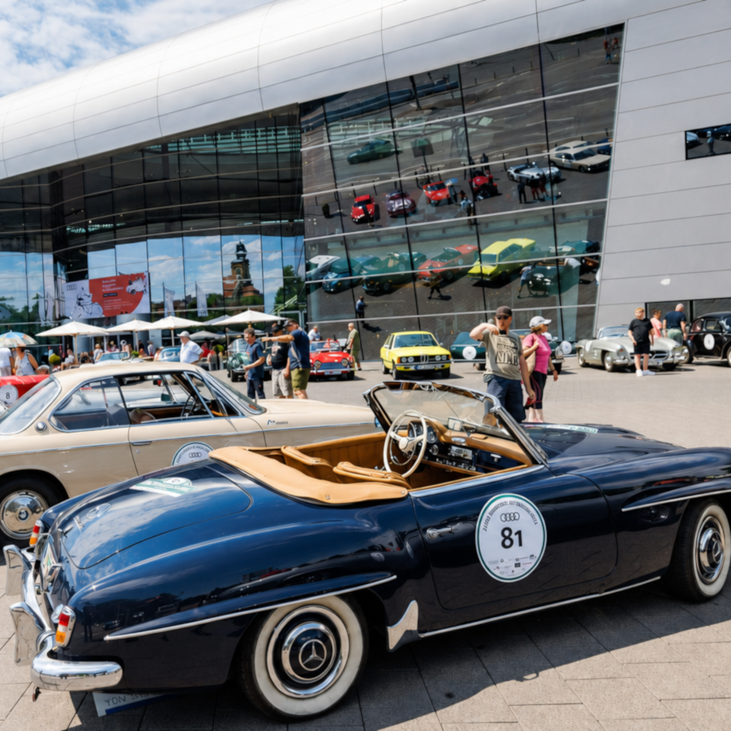 Klassische Oldtimer verschiedener Marken bei einem Treffen vor dem Audi Forum Neckarsulm mit Besuchern.