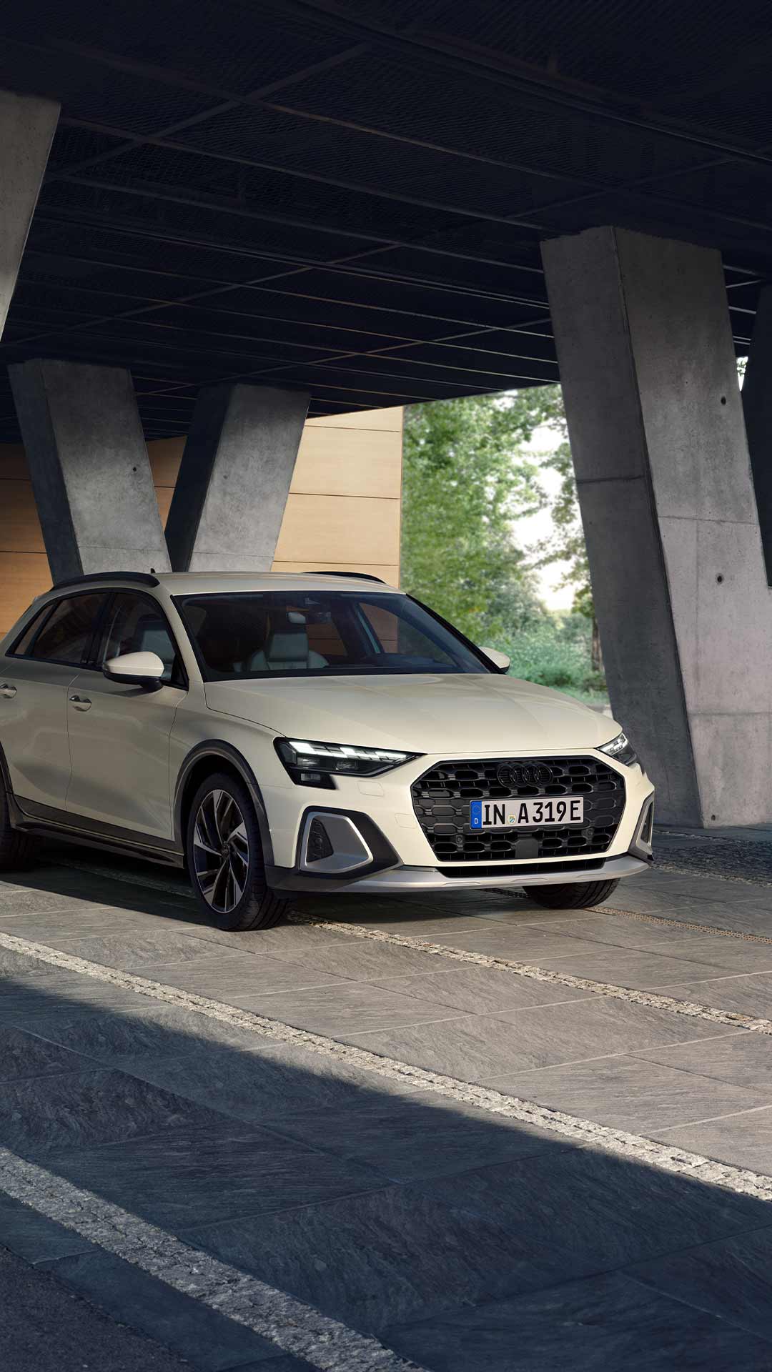 Frontansicht eines weißen Audi A3 allstreet TFSI e, geparkt unter moderner Betonarchitektur auf einem hellgrauen Steinboden.