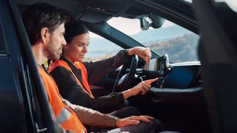 Zwei Personen mit Warnwesten bedienen Touchscreen im Audi, Berglandschaft im Hintergrund