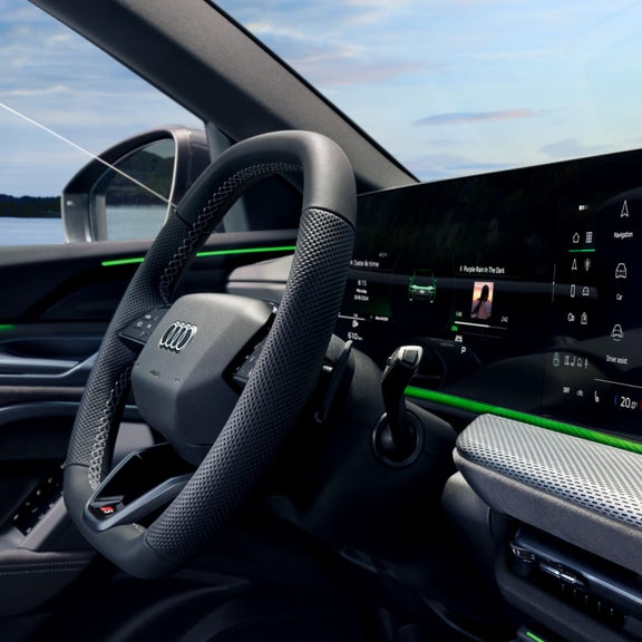 Car interior with a large touchscreen dashboard and steering wheel, with ocean view outside.