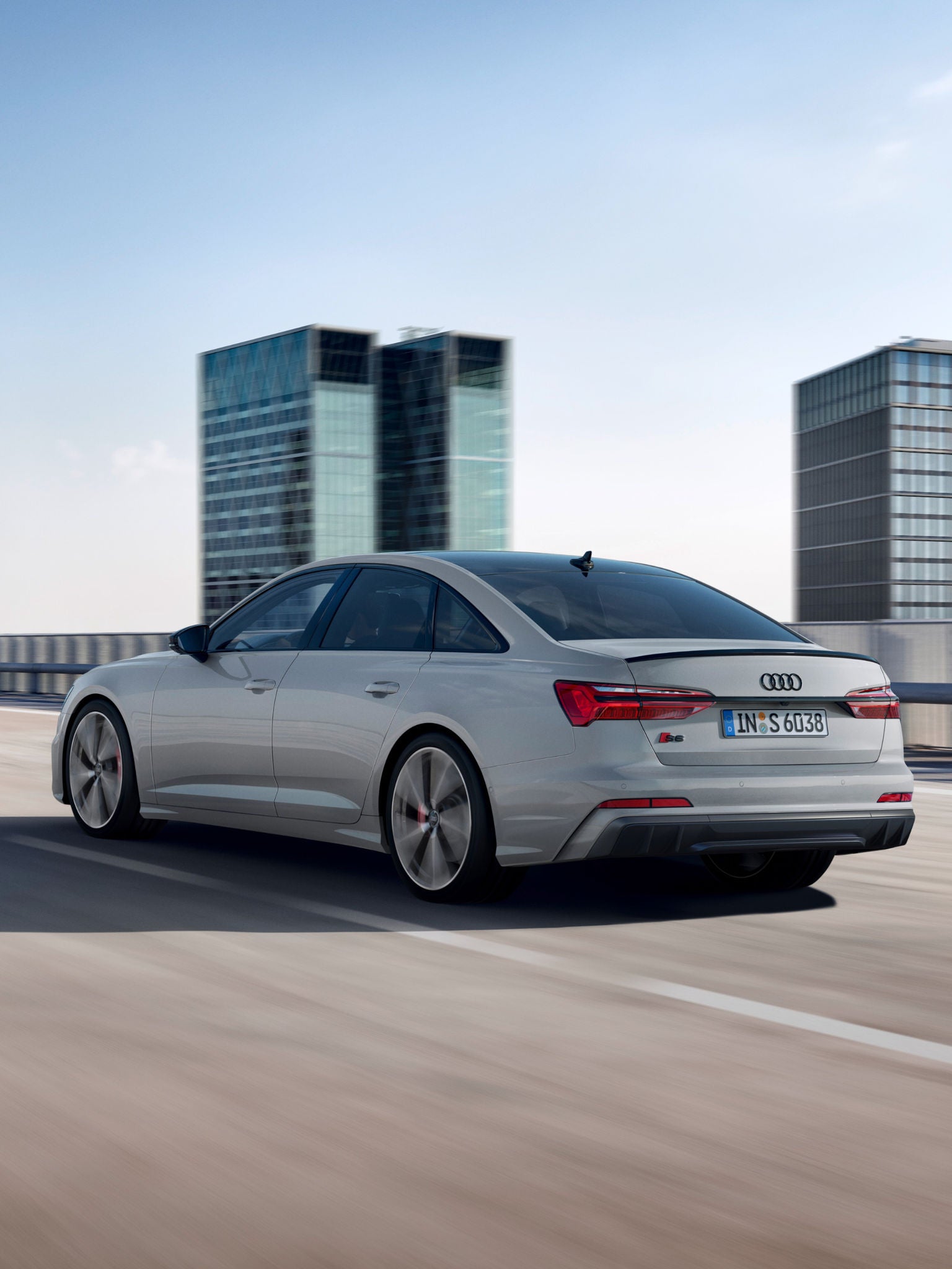 Silver sedan driving on highway with modern buildings in the background.