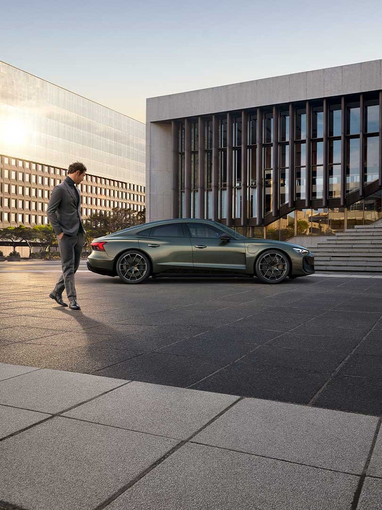 Ein Mann im Anzug geht am grünen Audi RS e-tron GT performance vorbei, der vor einem modernen Bürogebäude steht.