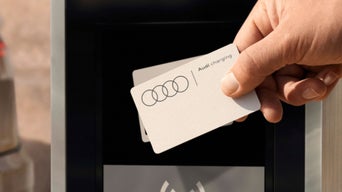 A hand holds an Audi charging card, poised to be tapped on a charging station screen.