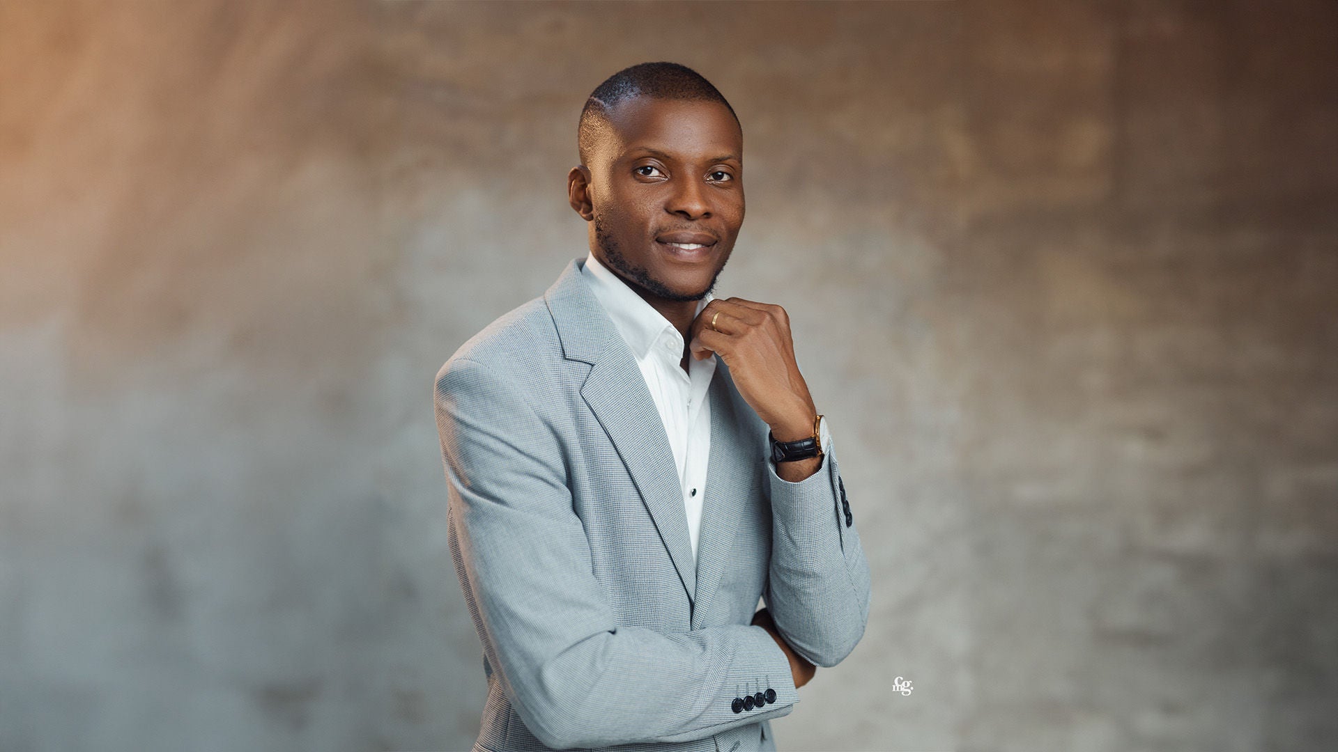 Mann im hellgrauen Anzug mit weißem Hemd, leicht lächelnd, vor neutralem Hintergrund.