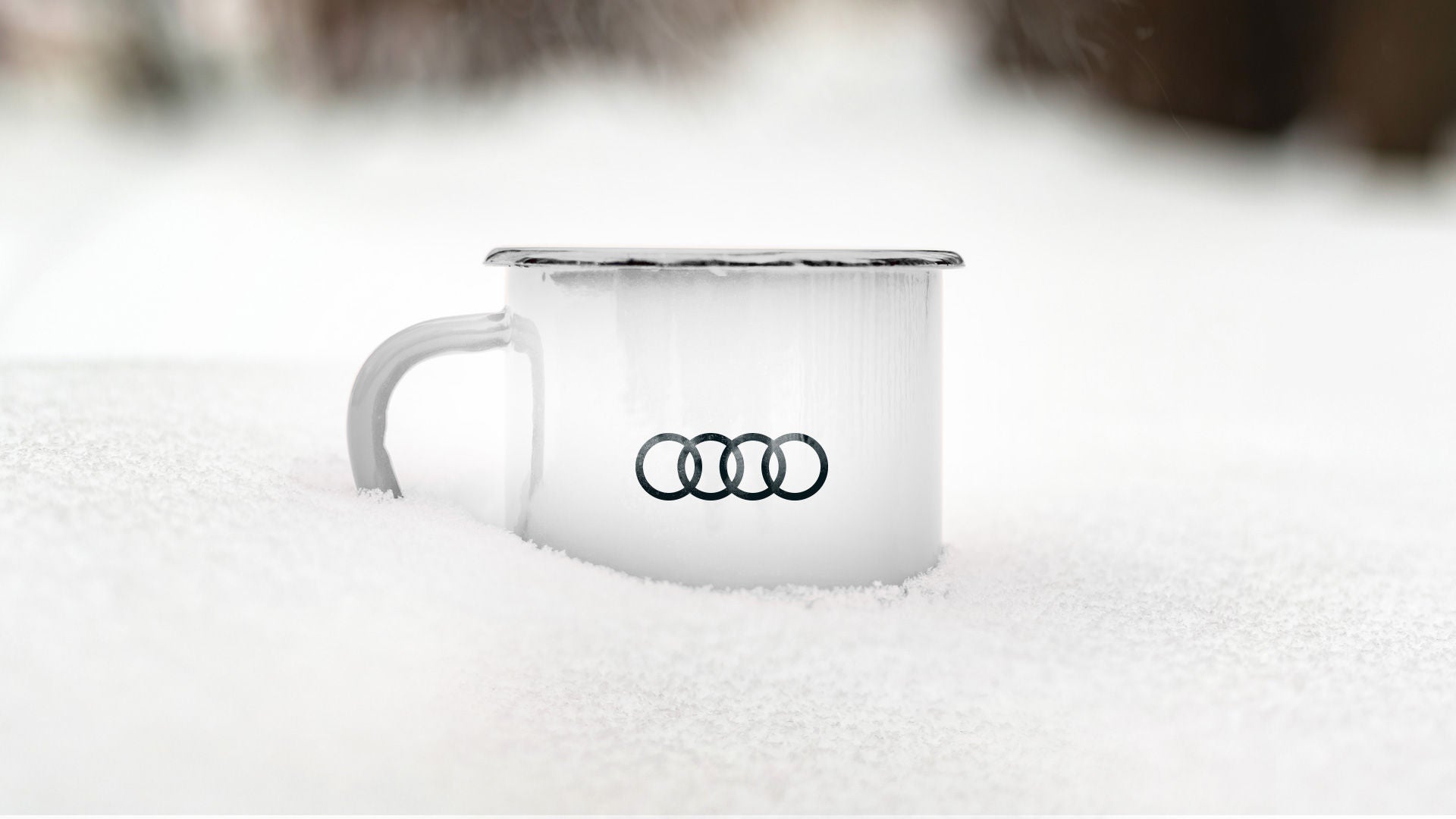 Eine weisse limierte Audi x DSV Tasse mit schwarzen Audi Ringen steht im Tiefschnee. Im Hintergrund sind schemenhaft Bäume zu erkennen