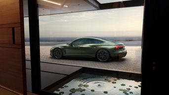 Seitenansicht eines metallic-grünen Audi RS e-tron GT performance vor großer Glasfront, im Vordergrund ein Wasserbecken mit Seerosen.