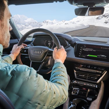 Driver's perspective inside an Audi car with snowy mountain scenery ahead.
